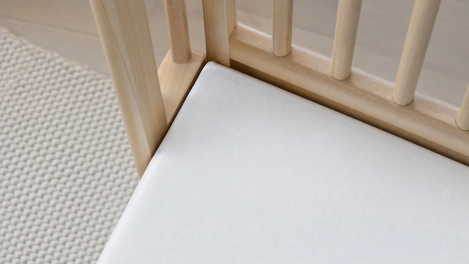 A close-up of a bare crib mattress fitted tightly against the crib slats with no gap at the corner